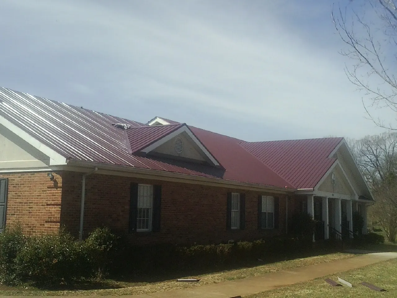 Red metal roof with gabled entries on a long brick building, from a Hail Damage Roof Repair job in Holt