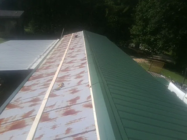 Old rusted panels beside newly installed green metal roofing — Wind Damage Roof Repair by Roofing Brothers in Holt