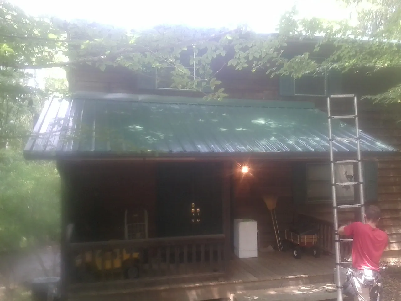 Worker on a ladder at the green porch roof of a wooded cabin in Holt