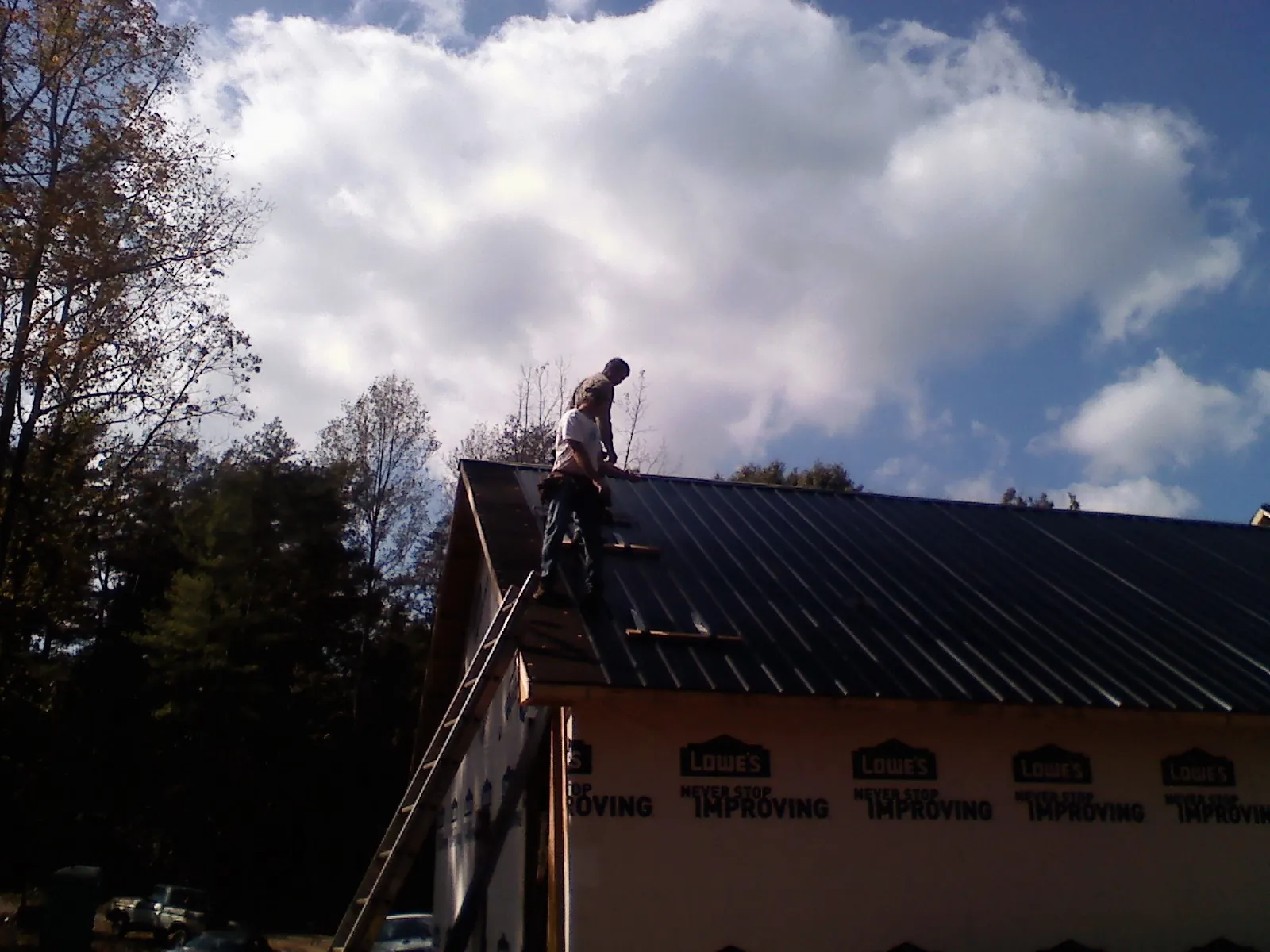 Roofer fastening dark metal panels high against a cloudy sky, from a Roof Inspection job in Holt