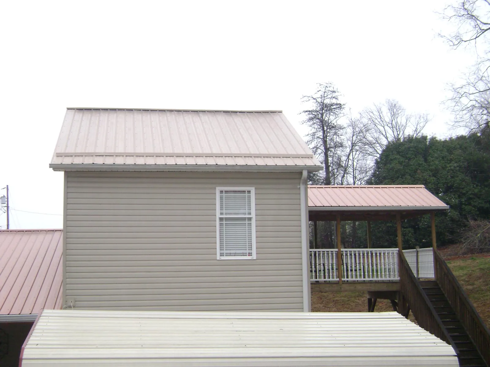 Tan metal roofs on a two story addition and attached porch, from a Roof Replacement job in Holt